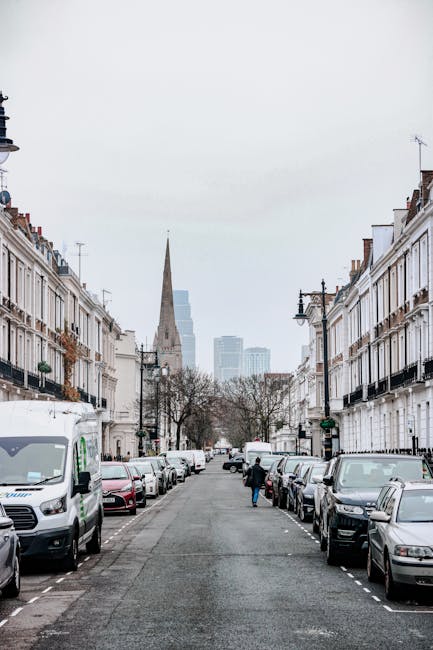 A wide view of a residential street on Finchley Road showing parked cars along both sides, including a silver Audi and several smaller vehicles. The street features traffic signs indicating a controll