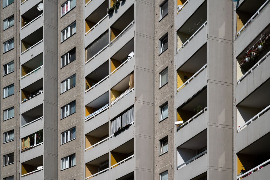 A high-rise residential building with multiple floors, each featuring large windows, some of which have partially open curtains or blinds. The exterior facade of the building is light-colored with hor
